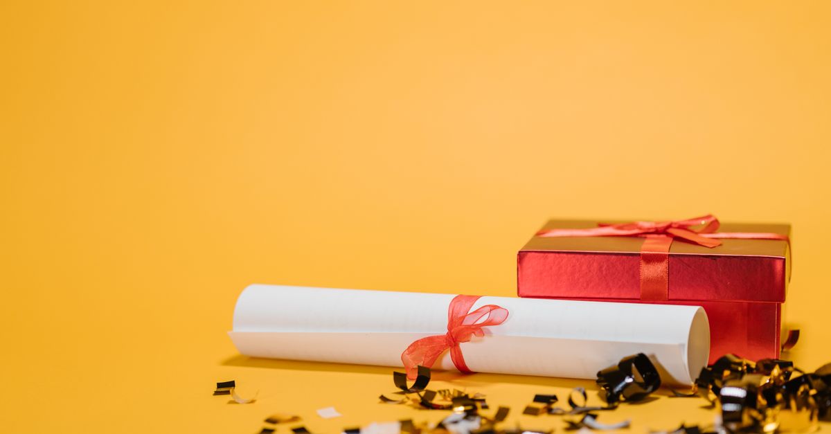 A red gift box and diploma with ribbons on a vibrant yellow background symbolizing celebration and achievement.